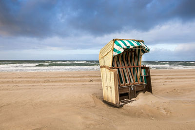 Hooded beach chair on beach against sky