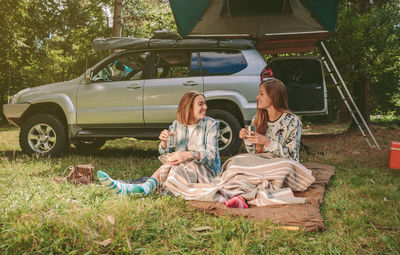 Smiling friends sitting at campsite in forest