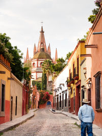 Rear view of man walking on footpath amidst buildings against la parroquia