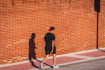 Man walking on footpath against red wall