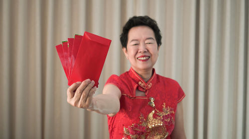 Portrait of smiling man holding red while standing against curtain