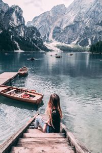 Woman sitting on jetty in lake against mountains