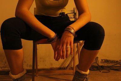 Midsection of woman sitting on chair against wall
