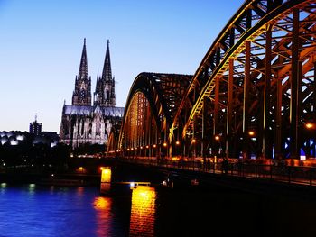 Illuminated bridge over river in city against clear sky