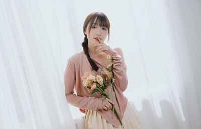 Portrait of young woman standing against curtain