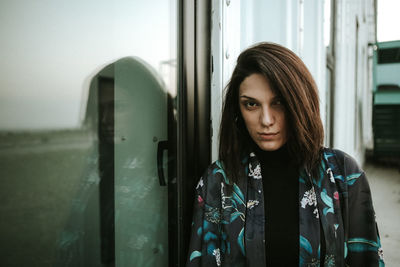 Portrait of young woman standing against window