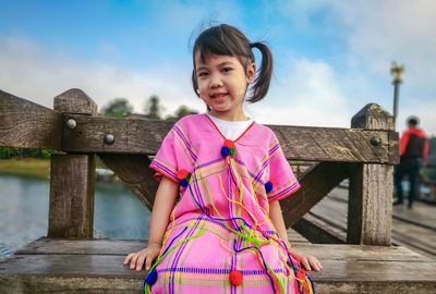 Portrait of girl sitting on pier over lake against sky