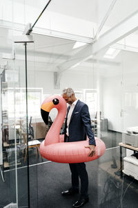 Happy businessman in office with inflatable flamingo