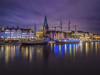 Illuminated city by river against sky at dusk