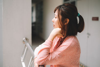 Thoughtful woman at railing in corridor looking away