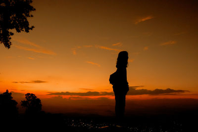 Silhouette woman standing on field against sky during sunset