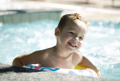 Happy boy with inflatable ring in swimming pool on sunny day