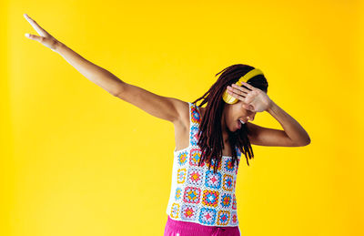 Portrait of young woman standing against yellow background