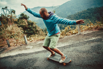 Mid adult man with arms outstretched skateboarding on road