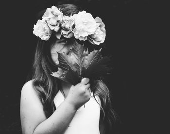 Portrait of girl covering face from flowers against black background