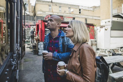 Couple holding disposable coffee shop standing outside store