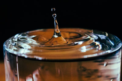 Close-up of water drop splashing in drinking glass against black background