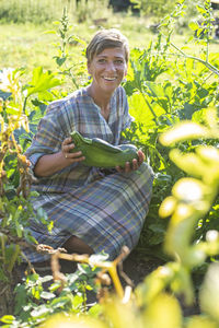 Portrait of smiling woman holding vegetable in hand at farm-