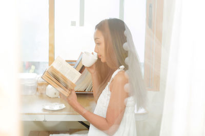 Side view of woman having coffee while reading book