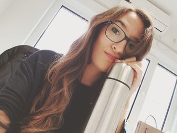 Portrait of young woman with long hair holding insulated drink container