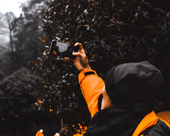 Rear view of man photographing camera on tree