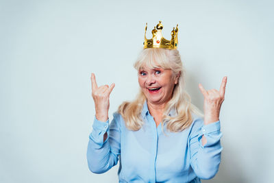 Portrait of smiling senior woman with crown against wall