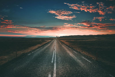 Road amidst field against sky during sunset