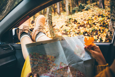 Woman legs stuck out of window reads map sits in automobile in a picturesque autumn forest 