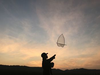 Silhouette man holding umbrella against sky during sunset