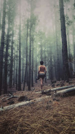 Full length of shirtless woman standing in forest during foggy weather