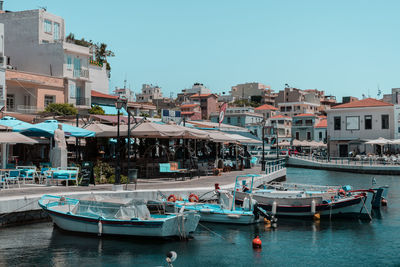 Boats moored at harbor by buildings against clear blue sky