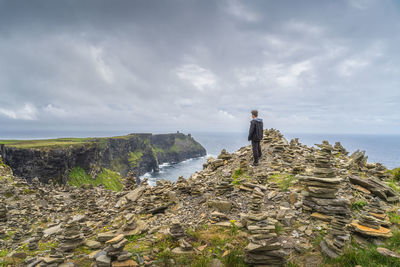 Man standing between stone stackings and admiring view on in iconic cliffs of moher, ireland