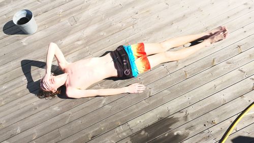 High angle view of shirtless teenage boy lying on pier