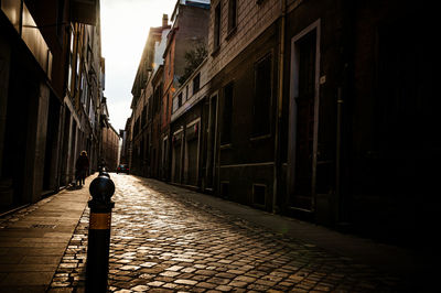 Rear view of man walking on narrow street amidst buildings