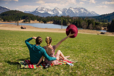 Rear view of couple sitting on field against mountain