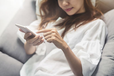 Midsection of woman using mobile phone on bed