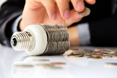 Midsection of man with light bulb and coins at table