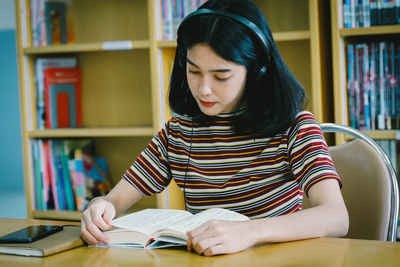 Young woman reading book while listening music on table