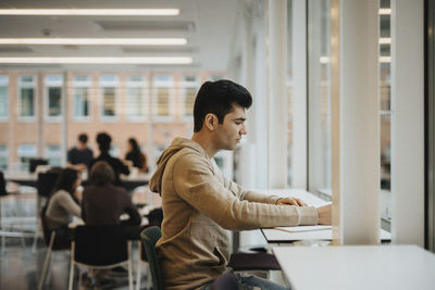 Side view of young male student studying at table in university