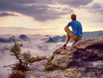 Autumnal morning in wild nature. hiker in sports wearing sit on sharp peak and watch natural show