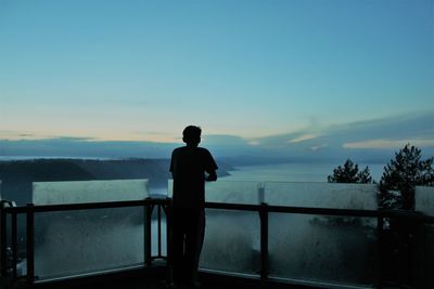 Rear view of silhouette man standing by railing against sky