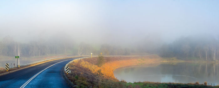 Road amidst trees against sky during foggy weather