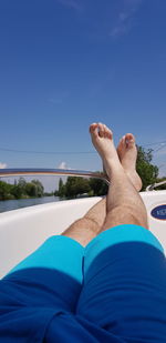 Low section of man relaxing against blue sky