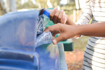 Cropped image of hands throwing crushed bottles in recycling bin