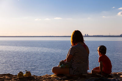 A young mother with her children boy and a newborn are sitting and enjoying the nature of the sea