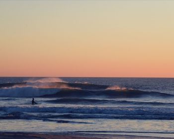 Silhouette man standing on beach against clear sky during sunset