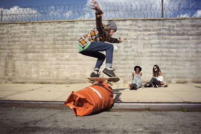 Young man performing skateboard stunt over barrel on street