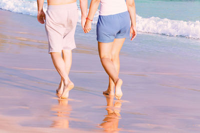 Couple holding hands is walking along the sandy sea beach. back bottom view