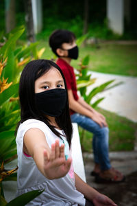 Two asian children wearing mask sitting in distance of 1 meter from others keeping distancing. 