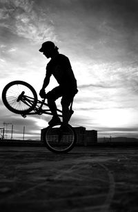 Silhouette man practicing stunt on bicycle against sky